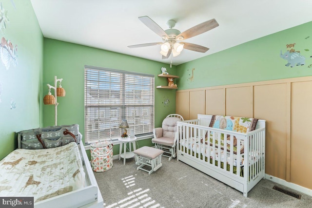 carpeted bedroom with ceiling fan and a crib