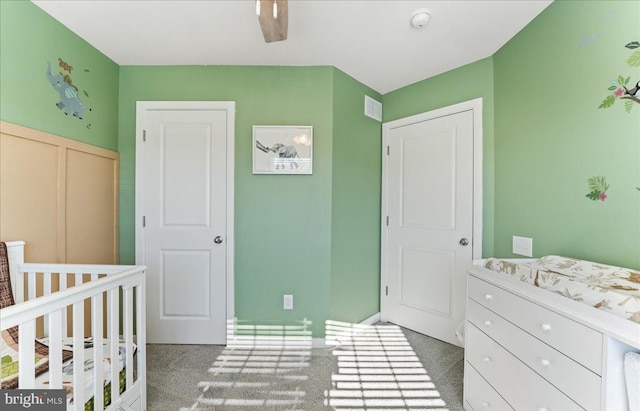 bedroom featuring dark colored carpet, ceiling fan, a crib, and a closet