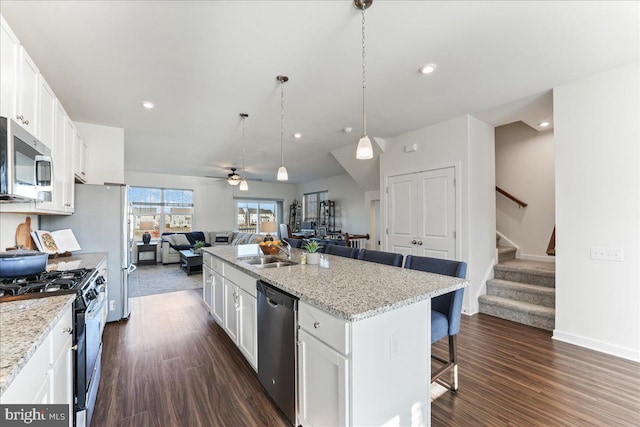 kitchen featuring a breakfast bar, white cabinets, a center island with sink, hanging light fixtures, and appliances with stainless steel finishes