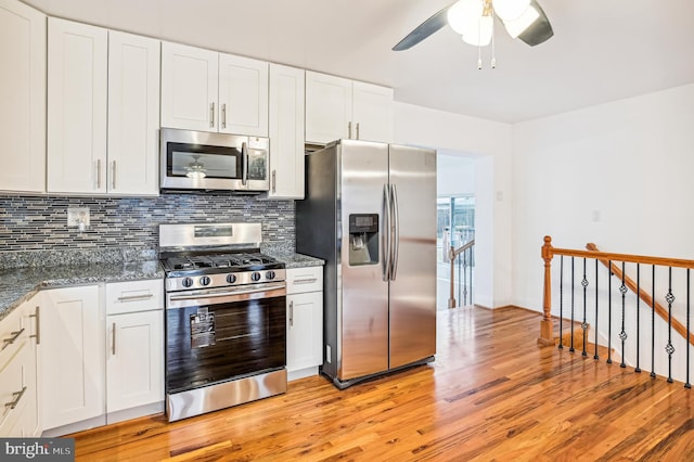 kitchen featuring stainless steel appliances, light hardwood / wood-style flooring, white cabinetry, and dark stone counters