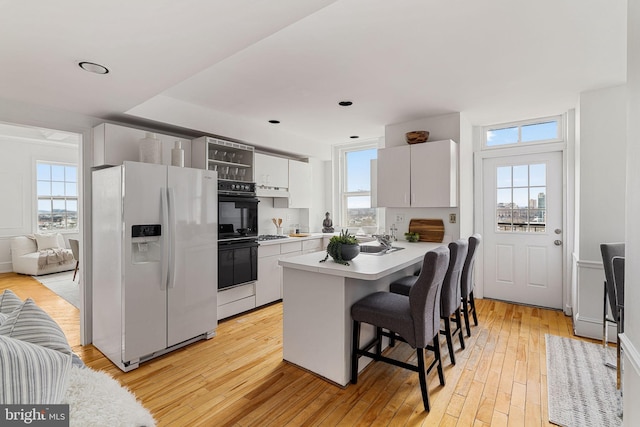 kitchen featuring a healthy amount of sunlight, light wood-type flooring, a kitchen breakfast bar, white refrigerator with ice dispenser, and white cabinets