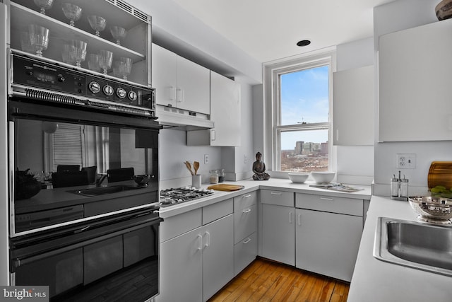 kitchen featuring light hardwood / wood-style floors, gray cabinets, stainless steel gas cooktop, double oven, and sink