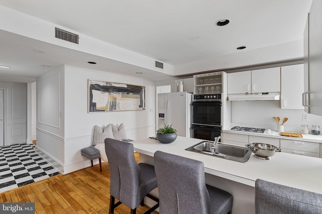 kitchen featuring a breakfast bar, gas cooktop, sink, white refrigerator with ice dispenser, and black double oven