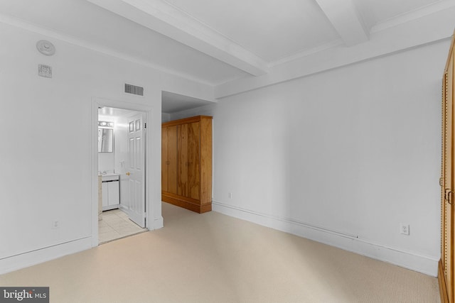 interior space with beam ceiling, light colored carpet, connected bathroom, and ornamental molding