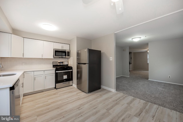 kitchen featuring stainless steel appliances, sink, white cabinets, light wood-type flooring, and decorative backsplash