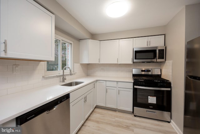 kitchen featuring decorative backsplash, sink, white cabinetry, light wood-type flooring, and appliances with stainless steel finishes