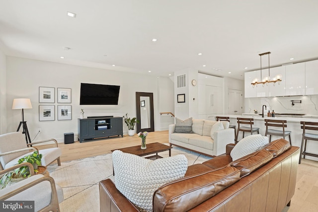 living room with sink, light wood-type flooring, and an inviting chandelier