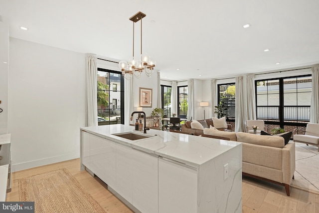 kitchen with light stone counters, a center island with sink, white cabinetry, hanging light fixtures, and sink