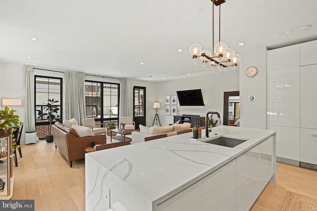 kitchen with white cabinets, a center island with sink, sink, and decorative light fixtures