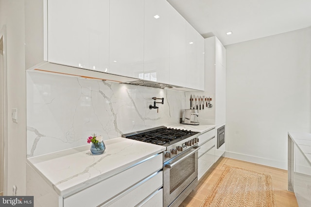 kitchen featuring white cabinetry, tasteful backsplash, light stone countertops, high end stove, and light hardwood / wood-style flooring