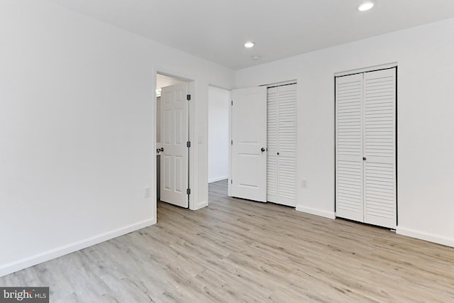 unfurnished bedroom with light hardwood / wood-style flooring and multiple closets