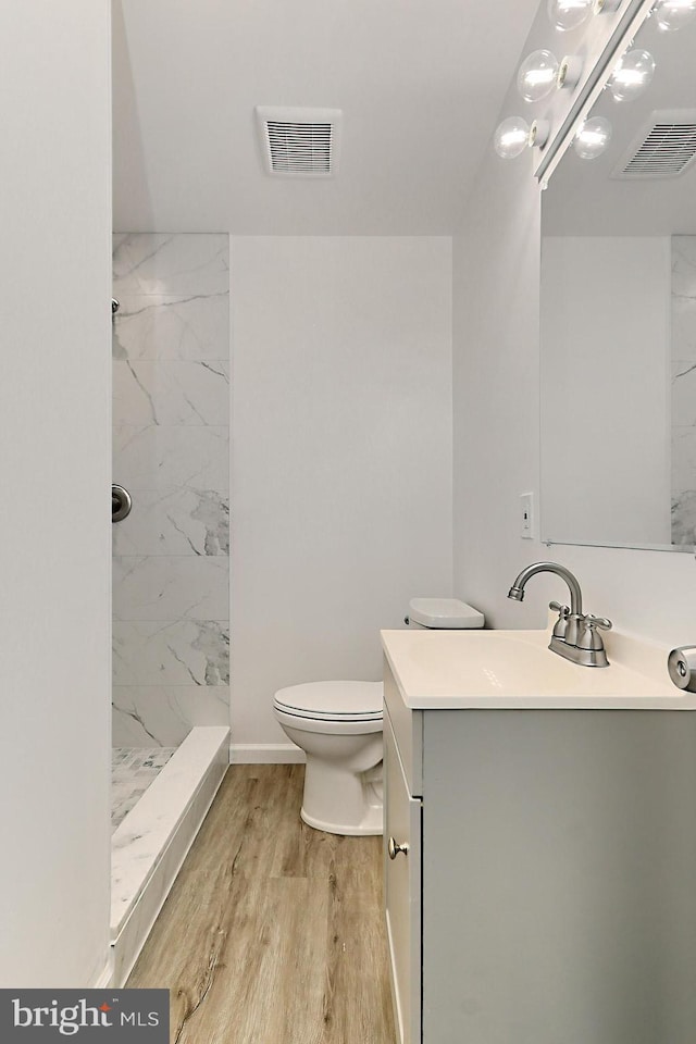 bathroom featuring hardwood / wood-style flooring, vanity, toilet, and tiled shower