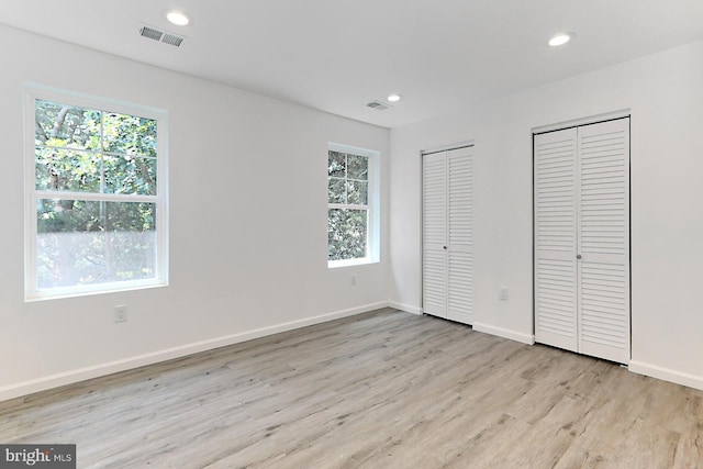 unfurnished bedroom with multiple closets and light hardwood / wood-style floors