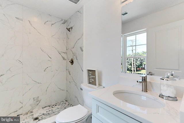 bathroom with a tile shower, vanity, and toilet