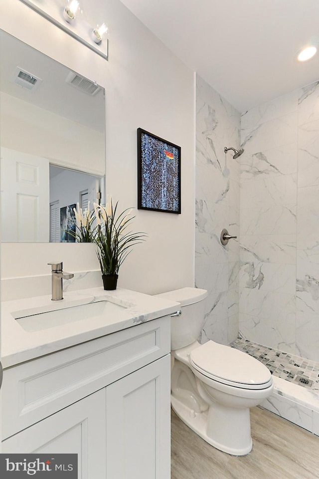 bathroom featuring tiled shower, vanity, hardwood / wood-style flooring, and toilet