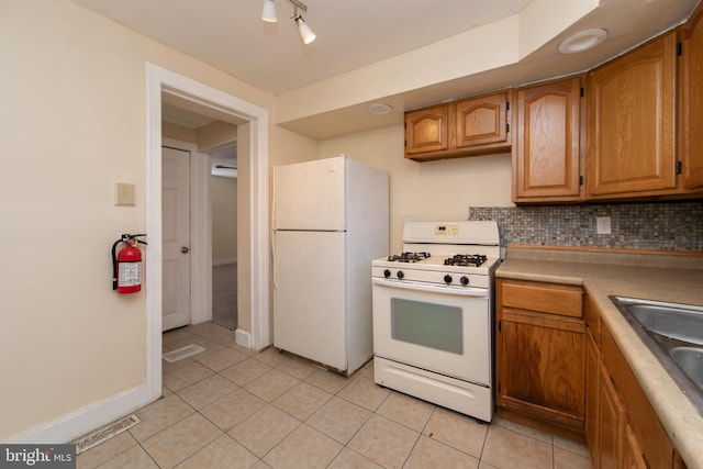 kitchen with sink, track lighting, white appliances, decorative backsplash, and light tile patterned floors