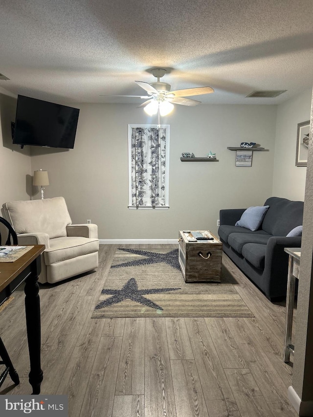 living room featuring ceiling fan, a textured ceiling, and light hardwood / wood-style flooring