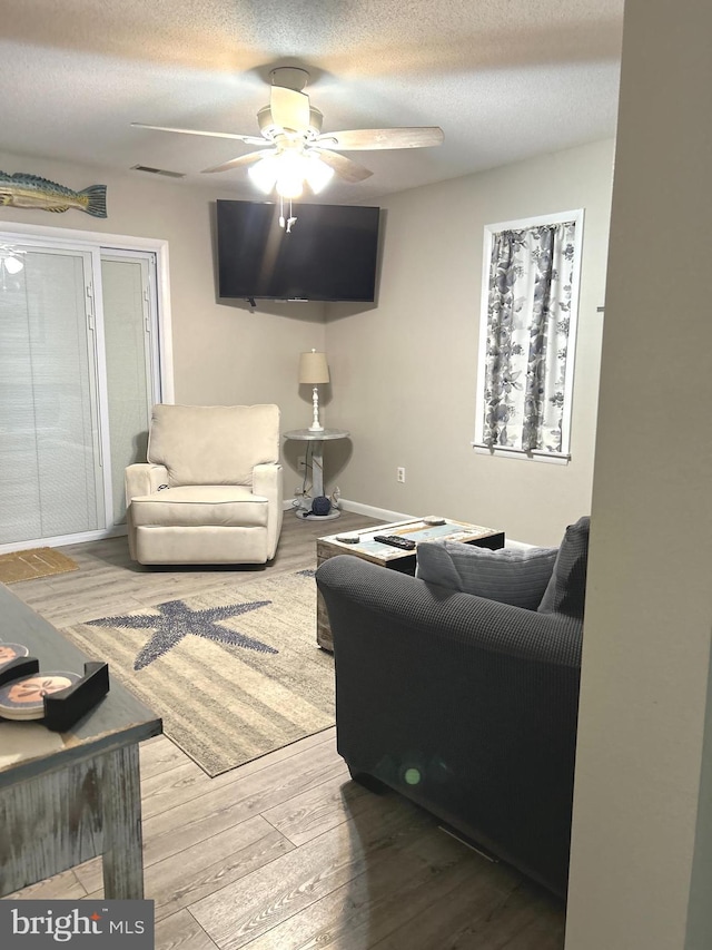 living room featuring light hardwood / wood-style floors, ceiling fan, and a textured ceiling