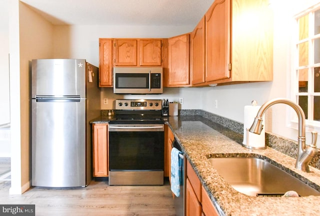 kitchen featuring appliances with stainless steel finishes, sink, light hardwood / wood-style floors, and stone countertops