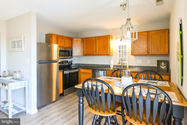 kitchen with stainless steel appliances, an inviting chandelier, hanging light fixtures, sink, and light hardwood / wood-style flooring