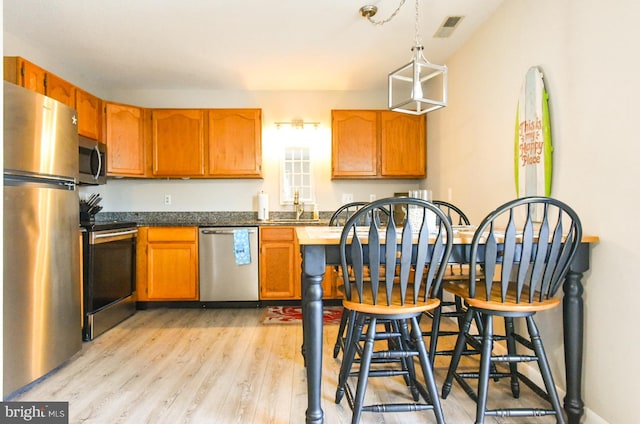 kitchen featuring sink, appliances with stainless steel finishes, decorative light fixtures, and light hardwood / wood-style flooring