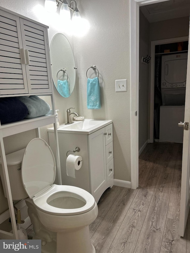 bathroom with hardwood / wood-style floors, vanity, toilet, and stacked washer / drying machine