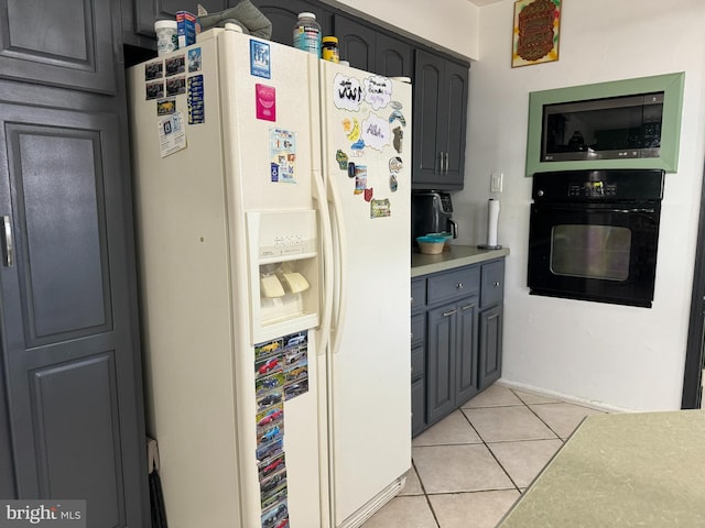 kitchen featuring light tile patterned flooring, oven, white refrigerator with ice dispenser, gray cabinets, and stainless steel microwave