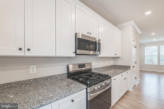 kitchen featuring crown molding, stainless steel appliances, white cabinetry, light stone countertops, and light hardwood / wood-style floors