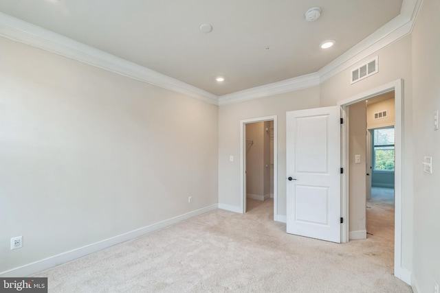 unfurnished bedroom with light colored carpet, a closet, a spacious closet, and ornamental molding