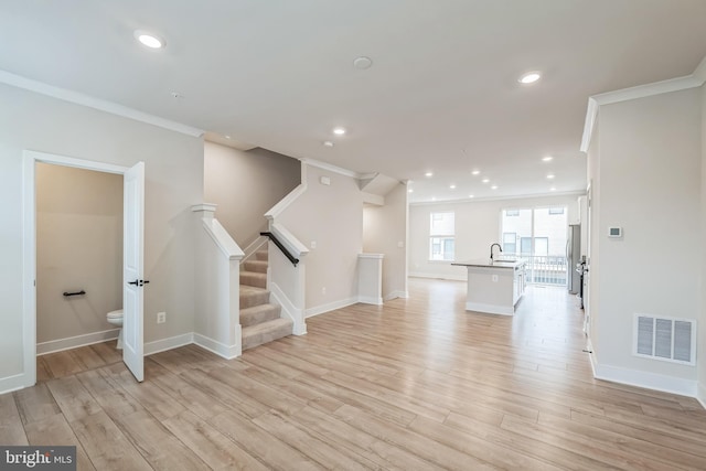 unfurnished living room featuring sink, light wood-type flooring, and ornamental molding