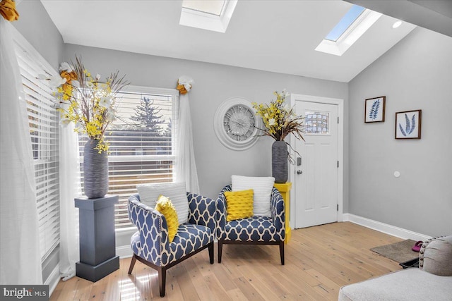 sitting room with a skylight, hardwood / wood-style floors, vaulted ceiling, and baseboards