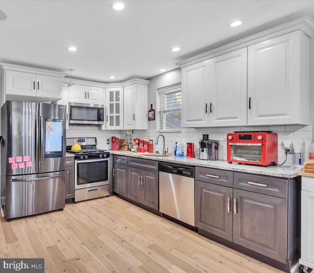 kitchen with stainless steel appliances, white cabinetry, sink, light stone countertops, and light hardwood / wood-style flooring