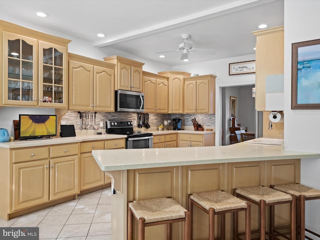 kitchen with light brown cabinetry, kitchen peninsula, appliances with stainless steel finishes, and a breakfast bar area