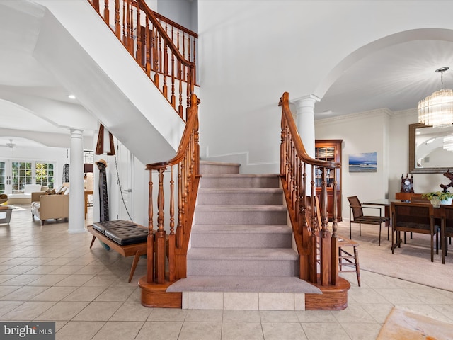 staircase featuring tile patterned flooring, a notable chandelier, ornate columns, and crown molding