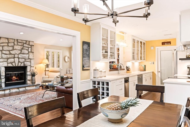 dining area featuring wood-type flooring, a notable chandelier, sink, ornamental molding, and a fireplace