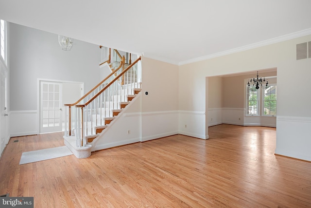 unfurnished living room with a notable chandelier, ornamental molding, and light wood-type flooring