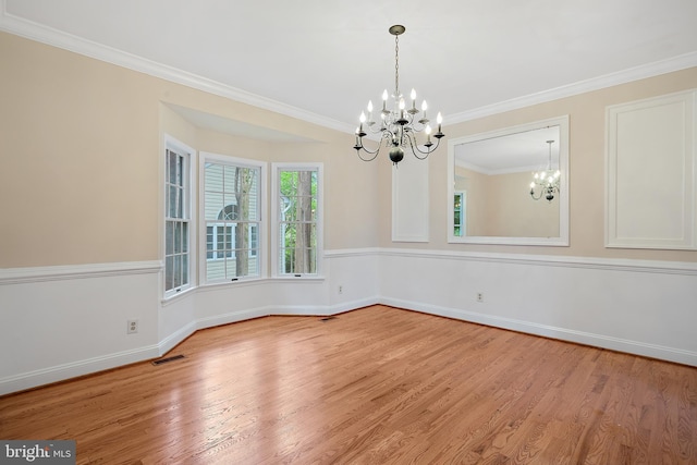 empty room featuring hardwood / wood-style flooring, crown molding, and a chandelier