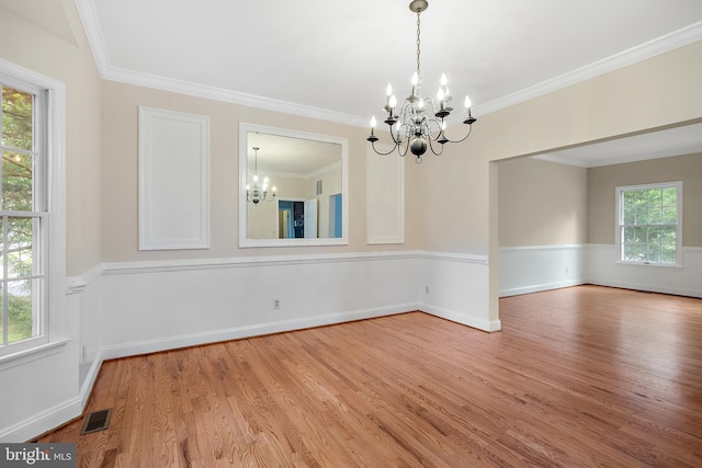 unfurnished dining area with hardwood / wood-style flooring, crown molding, plenty of natural light, and a notable chandelier