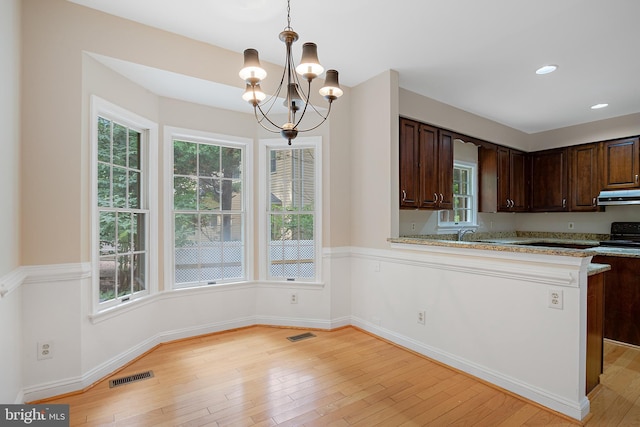 kitchen featuring range hood, hanging light fixtures, light stone counters, kitchen peninsula, and dark brown cabinetry