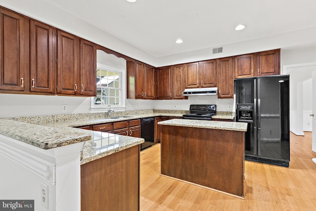 kitchen featuring sink, light wood-type flooring, a kitchen island, light stone countertops, and black appliances