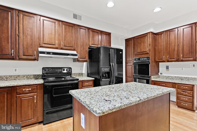 kitchen featuring a center island, light wood-type flooring, light stone countertops, and black appliances