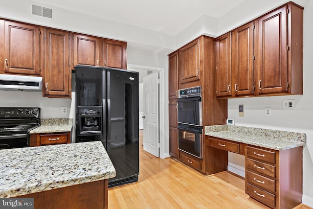 kitchen with light stone counters, extractor fan, built in desk, and black appliances