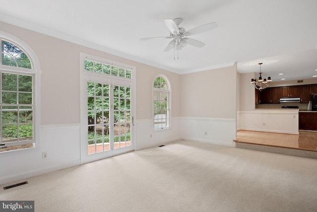 unfurnished living room featuring crown molding, ceiling fan with notable chandelier, and light colored carpet