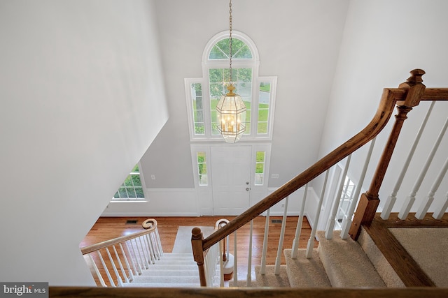 staircase featuring a high ceiling, hardwood / wood-style flooring, and a notable chandelier