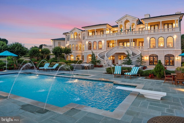 back house at dusk with pool water feature, a patio area, and a balcony