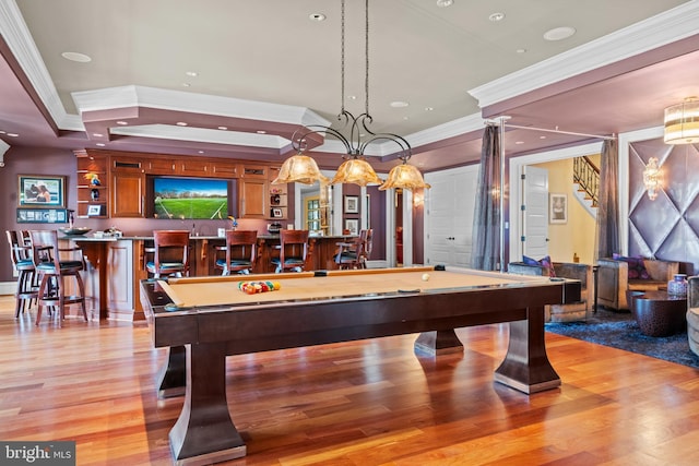 game room with light hardwood / wood-style floors, billiards, a raised ceiling, ornamental molding, and bar area