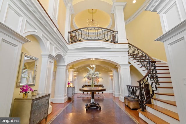 entrance foyer with a towering ceiling, crown molding, a chandelier, and decorative columns