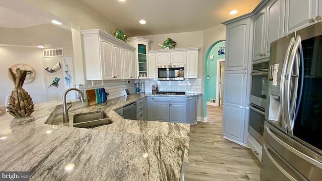 kitchen featuring white cabinetry, sink, light stone counters, appliances with stainless steel finishes, and light hardwood / wood-style flooring