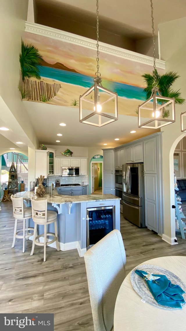 kitchen with gray cabinetry, wine cooler, backsplash, appliances with stainless steel finishes, and hanging light fixtures