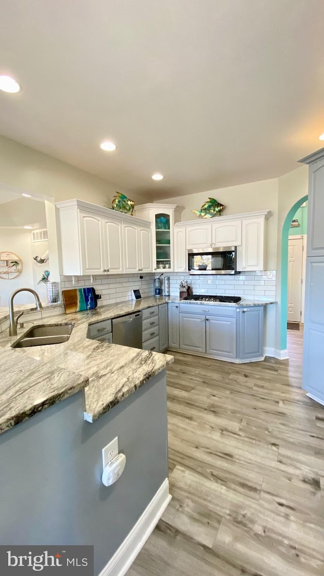 kitchen with light stone counters, stainless steel appliances, white cabinetry, sink, and kitchen peninsula